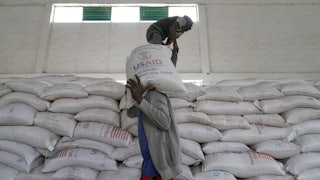 Aid workers in Ethiopia move large bags of yellow lentils labelled USAID. (There is a giant wall of them.)
