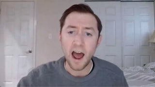 Justin Mohns (a white, young man with brown hair) is in a bedroom yelling at the camera. He wears a gray sweater. Behind him is a white comforter, and three sets of doors.