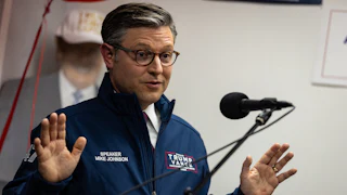 Mike Johnson holds his hands up while speaking into a microphone