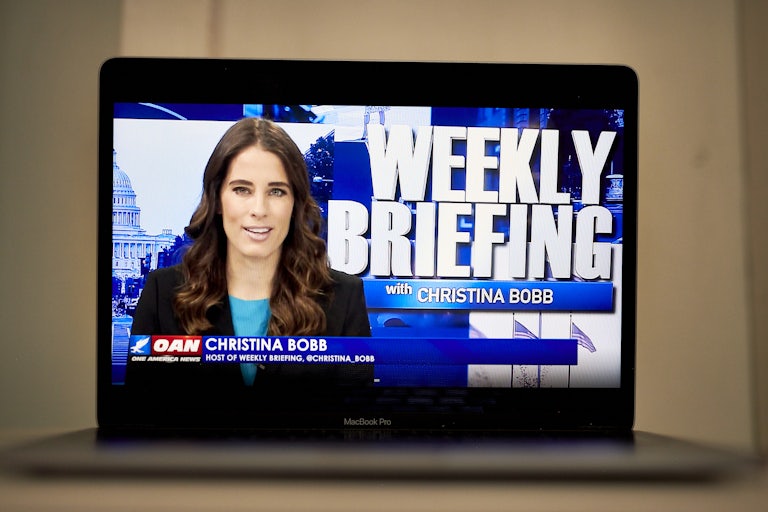A laptop computer shows Christian Bobb and the words "Weekly Briefing with Christina Bobb" on OANN.