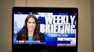 A laptop computer shows Christian Bobb and the words "Weekly Briefing with Christina Bobb" on OANN.