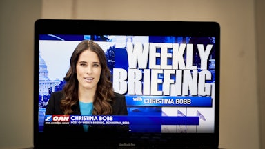 A laptop computer shows Christian Bobb and the words "Weekly Briefing with Christina Bobb" on OANN.