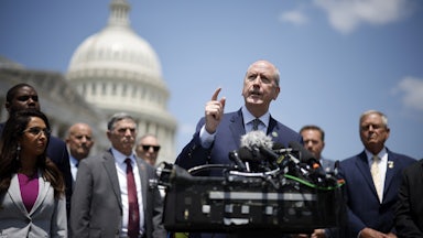 Dan Bishop speaks at a podium with other Freedom Caucus members and the U.S. Capitol in the background.