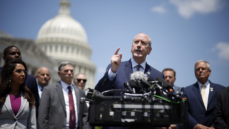Dan Bishop speaks at a podium with other Freedom Caucus members and the U.S. Capitol in the background.