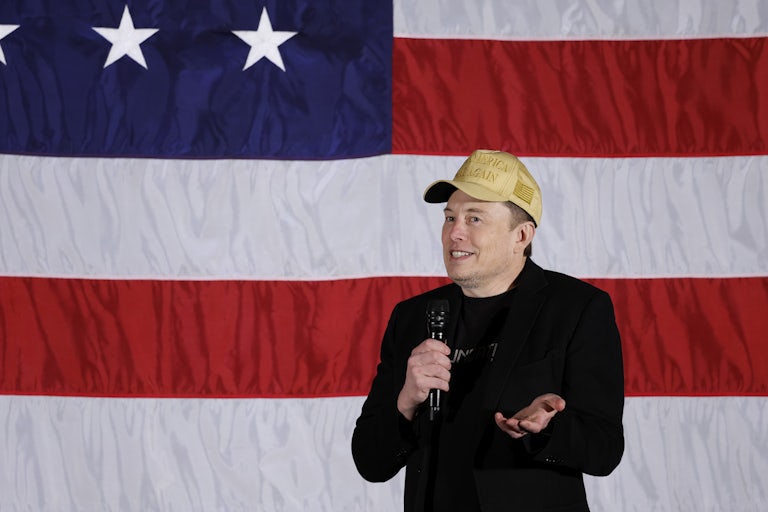 Elon Musk shrugs and holds up a microphone while speaking at a Donald Trump event