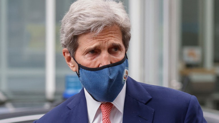 Climate envoy John Kerry, wearing a face mask, looks to the side.