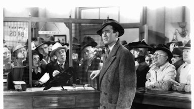 James Stewart standing in the cashier cubicle of a bank in a scene from the film 'It's A Wonderful Life', 1946.