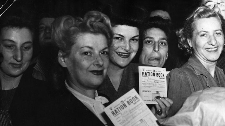 Women hold up their ration books while smiling.