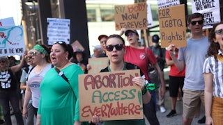 A protester holds a sign reading "Abortion Access Everywhere!" in a group featuring a number of pro-abortion and pro-LGBTQ rights signs.