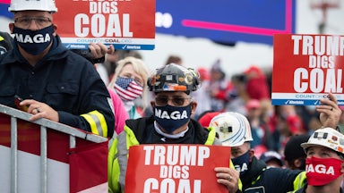 People in hard hats hold signs saying "Trump digs coal."