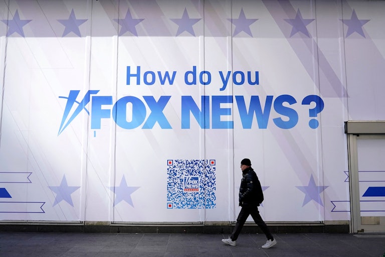 A person walks past the Fox News headquarters. The wall reads: "How do you Fox News?" alongside a giant QR code.