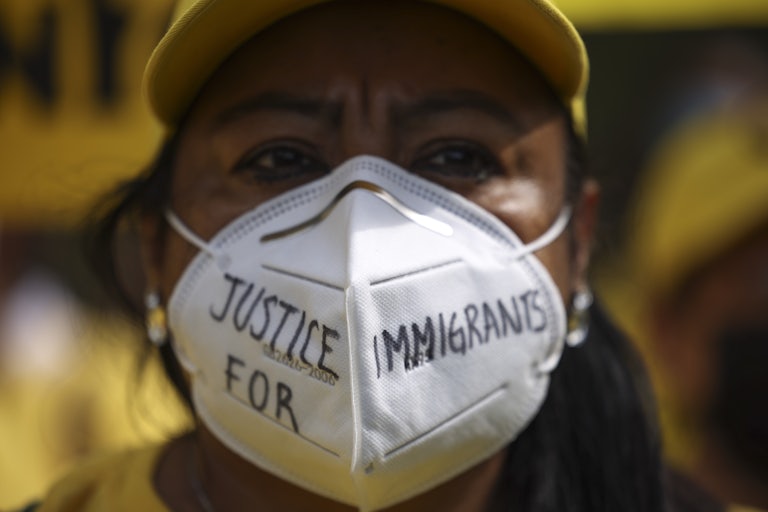 A darker skinned woman wears a mask that says "Justice for Immigrants."