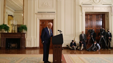 President Joe Biden stands behind a lectern, looking down at the floor.