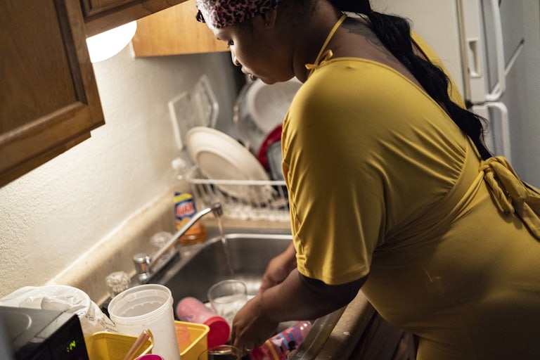 A woman moves dishes out of a sink with the water running.