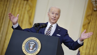 President Joe Biden stands behind a lectern, shrugging.