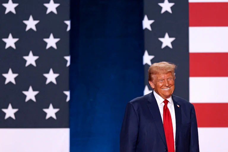 Donald Trump smiles in front of U.S. flags