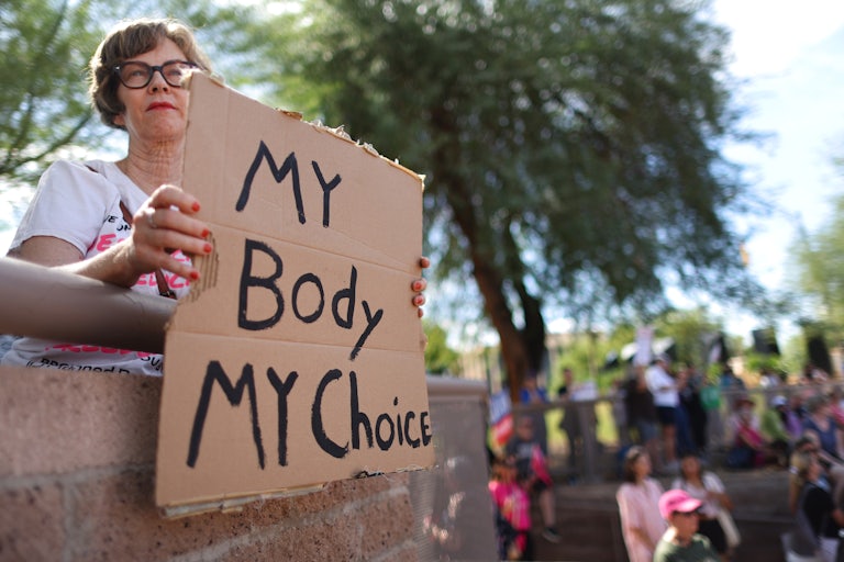 A woman outside holds a sign that reads "My body my choice."