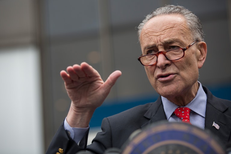 Senator Chuck Schumer extends his hand, gesticulating at a press conference.