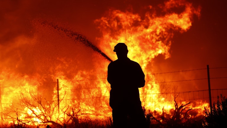  A utility worker uses a hose to extinguish a fire near power poles as the Dixie Fire moves near Janesville, California.
