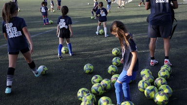 Children kick soccer balls on artificial turf.