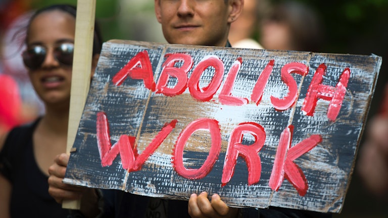 A May Day demonstrator holds a sign that reads "Abolish Work"