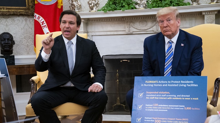 Florida Governor Ron DeSantis gesticulates while speaking as President Donald Trump looks on.