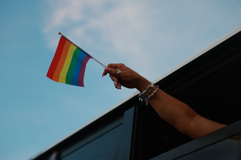 A hand outside a inwdow hold a pride flag in the wind