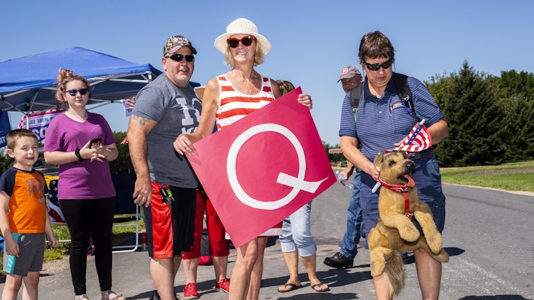 QAnon supporters hold a "Q" banner at a Trump campaign stop this summer.