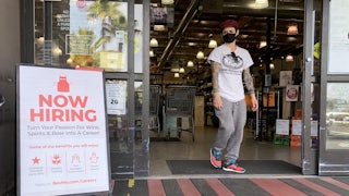 A masked customer walks past a "Now Hiring" sign outside a BevMo store in Larkspur, California.