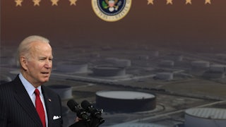 President Biden speaks in front of a backdrop depicting industrial storage tanks.