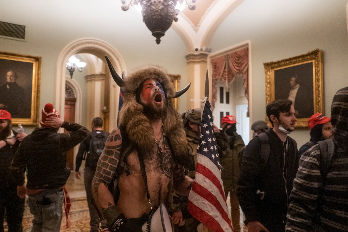 The "QAnon Shaman" pictured wearing a horned fur hat, face paint and carrying an American flag, shouting inside the U.S. Capitol in the first moments after the mob breached the building on January 6, 2021.