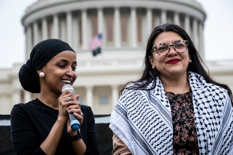 Ilhan Omar speaks into a microphone while standing next to Rashida Tlaib in front of the U.S. Capitol