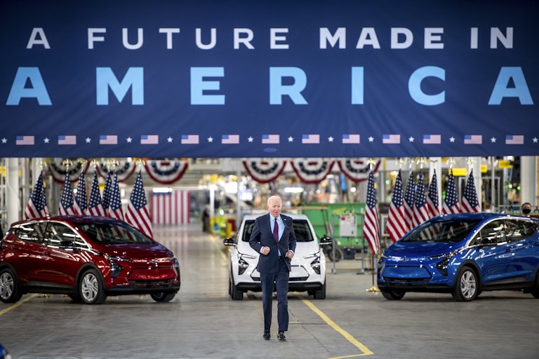 President Biden walks in front of red, white, and blue cars.