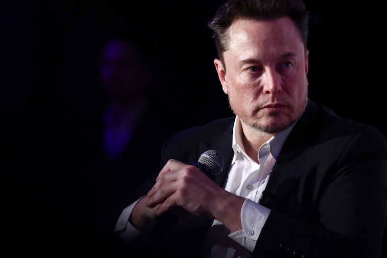 Elon Musks holds a microphone while seated.