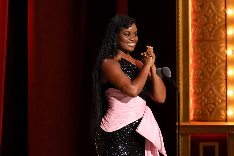 Denée Benton clasps her hands together at the mic onstage