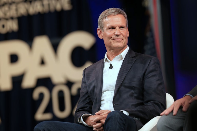 Tennessee Governor Bill Lee is seated on stage and smiles. The words CPAC appear behind him.