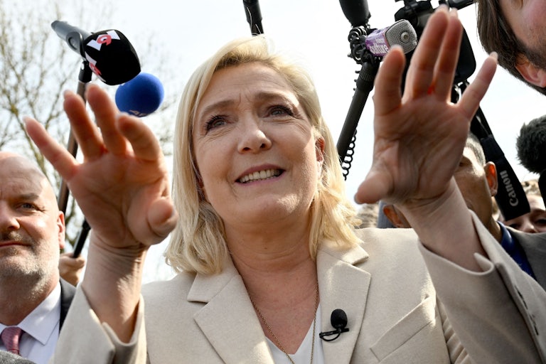 Marine Le Pen gesticulates while speaking, with microphones in her face.