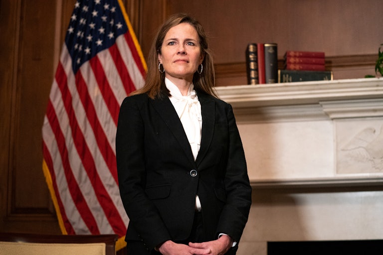 Supreme Court Justice Amy Coney Barrett stands in front of an American flag.