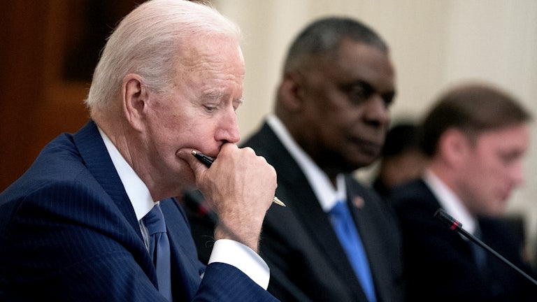 President Biden sits at a table with a pen and his chin in his hand.