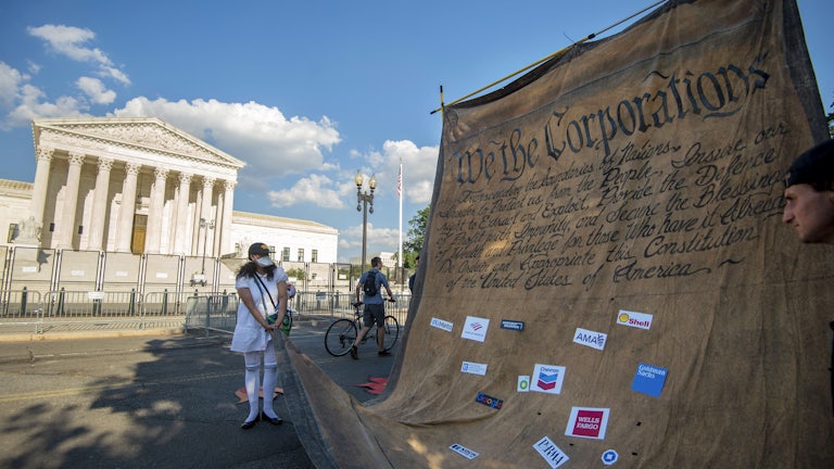 Climate activists carry a giant model of the constitution, altered to say "We The Corporations," in front of the Supreme Court building in Washington, D.C.
