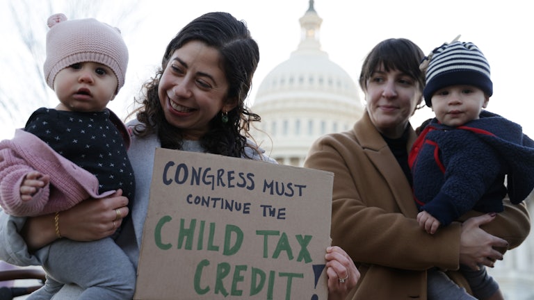 Two mothers hold their infant children and a sign in support of the child tax credit at a rally in Washington.