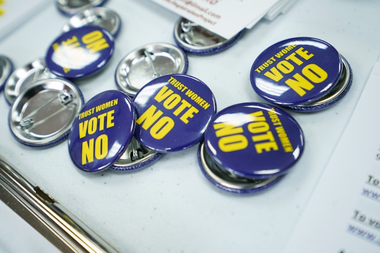 "Trust Women Vote No" pins scattered on a table
