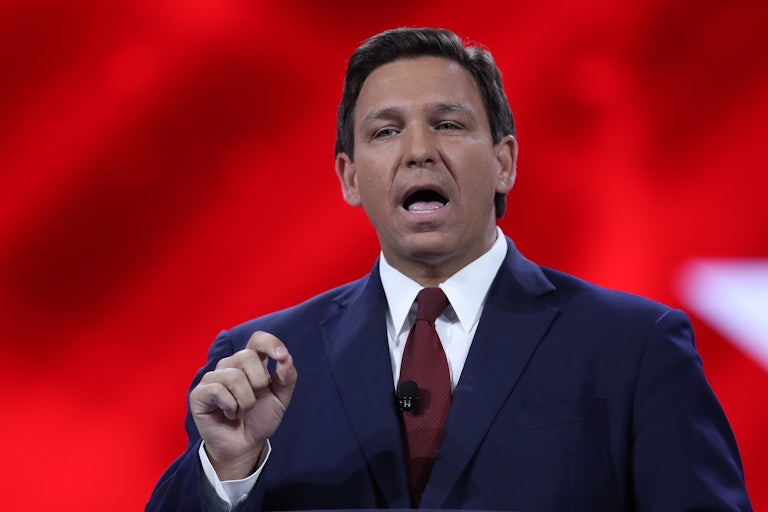 A close up of Ron DeSantis speaking to an audience in front of a red background.