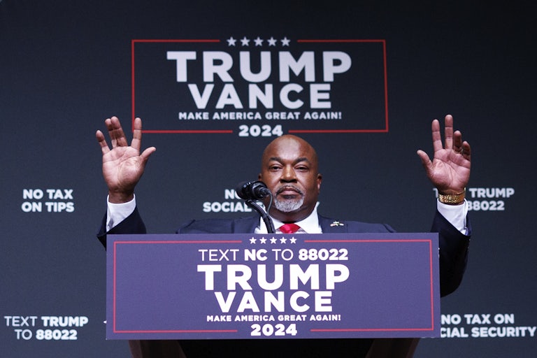 Mark Robinson holds his hands up while standing at a podium during a Donald Trump campaign event