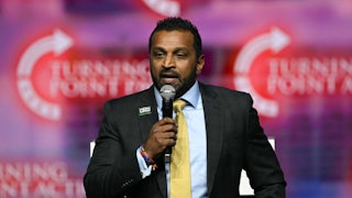 Kash Patel holds up a microphone and speaks into it