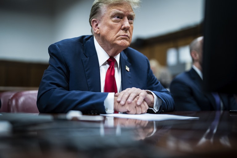 Donald Trump, seen in three-quarter profile, looks ahead while sitting at a table with his hands folded