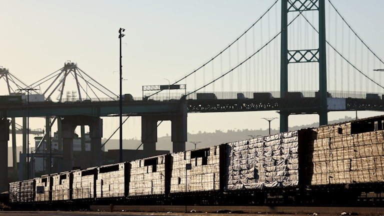 Loaded freight cars sit beneath a bridge.