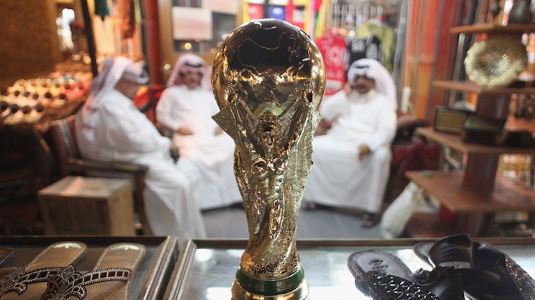 Men sit at a shoemaker's stall with a replica of the FIFA World Cup trophy in the Souq Waqif traditional market in Doha, Qatar.