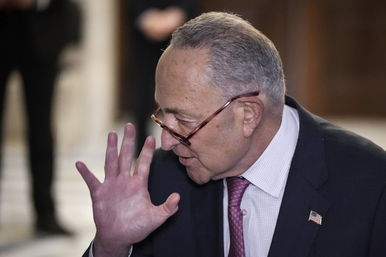 Chuck Schumer holds his hand up.
