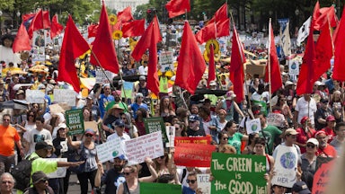 Protesters fill the streets in front of the Capitol, holding signs and waving red flags.